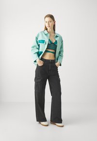 Giacca oversize azzurro chiaro con tasche, pantaloni cargo neri, bralette turchese e scarpe bianche con suola beige. Texture liscia, design moderno.