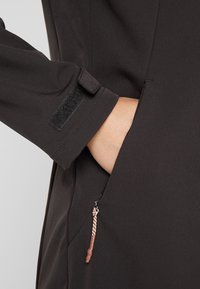 Chaqueta negra con un bolsillo con cremallera y un tirador texturizado, y cierre de puño de Velcro. Tela suave y ligera.