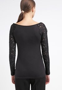 Černý top s dlouhými krajkovými rukávy, kulatým výstřihem, přiléhavým střihem, hladkým tělovým materiálem a detailním krajkovým vzorem na rukávech.