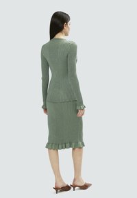 Completo a due pezzi in maglia a coste di un verde tenue, caratterizzato da un top aderente con scollatura a giro e una gonna di lunghezza media con orlo arricciato.
