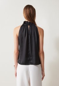 Il top halter in satin nero presenta un collo arricciato e un'apertura a chiave sul retro. La texture liscia e la vestibilità comoda completano il design.