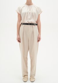 Lys beige top med plissee, parret med højtaljede beige bukser og et sort bælte. Fodtøjet har et glat, lyse farvet design.