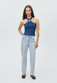 Navy ribbed crop top with halter neck and circular cutout, paired with light blue straight-leg jeans and dark blue slip-on shoes.