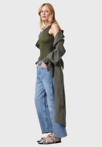 Olivovo-zelený rebrovaný top, svetlošedý trench coat, široké denimmové nohavice a vzorované slip-on topánky s detailom pracky.