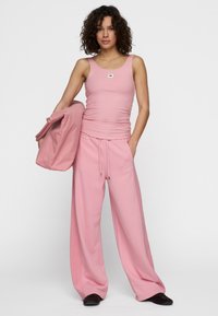 Roze geribbelde tanktop en wijde broek van zacht materiaal, gecombineerd met een bijpassende roze jas met een klein logo-detail.