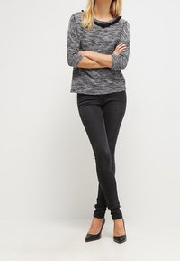 Schwarze, taillierte Jeans kombiniert mit einem strukturierten grauen Pullover mit weitem Ausschnitt und Dreiviertelärmeln. Stilettos runden das Outfit ab.