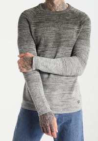 Grauer Strickpullover mit strukturiertem Muster, rundem Ausschnitt und langen Ärmeln, kombiniert mit blauer Jeans. Lässiges Design mit gerippten Bündchen.