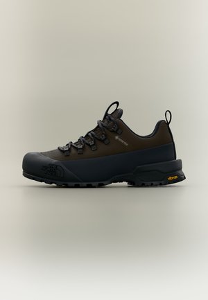 Chaussure de randonnée basse noire et marron foncé avec crochets pour lacets, étiquette Gore-Tex, semelle épaisse et logo Vibram au talon.