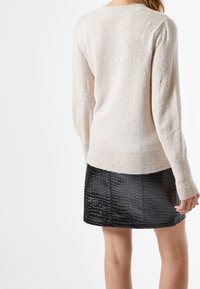 Brede, beige trui met een textuurafwerking en subtiele glans, gecombineerd met een zwarte leren minirok met een krokodillenpatroon.