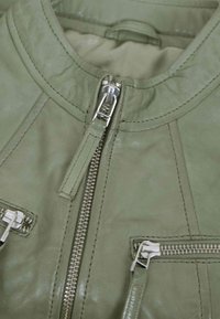 Close-up of olive green leather jacket showing a vertical zipper with pull tab and two horizontal zippered pockets with metal hardware.