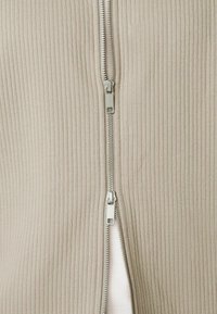 Nahaufnahme eines beigen, gerippten Stoffs mit einem silbernen Doppelreißverschluss, der in der Mitte teilweise geöffnet ist.