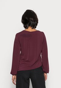 Burgundowy longsleeve z okrągłym dekoltem i teksturowanym materiałem, cechujący się luźnym krojem i marszczeniami z tyłu.