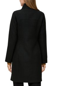 Zwarte wollen jas met een hoge kraag, lange mouwen en een getailleerde pasvorm. Bevat een gestructureerde afwerking en strakke lijnen, geschikt voor formele kleding.