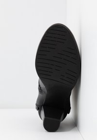 Stivale in pelle nera con suola in gomma texture, tacco basso e cuciture decorative lungo i lati, visto dal basso.