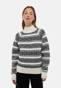Pull en maille noir et blanc, avec des motifs géométriques, un col haut, des poignets côtelés et un ourlet, fabriqué en tissu doux avec une finition texturée.