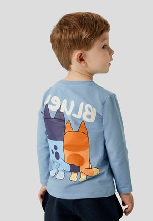 Jasnoniebieska koszula z długim rękawem z kreskówkowym motywem trzech ogonów psów na plecach, z białym napisem "BLUE" powyżej.