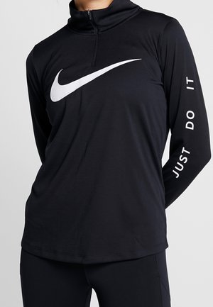 Schwarzes langärmliges Sportoberteil mit weißem Nike-Swoosh auf der Brust und dem Schriftzug "Just Do It" auf dem rechten Ärmel, getragen von einer Person.