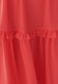 Kanka koraali chiffon-kangas, jossa on röyhelöhelma. Kankaan rakenne on kevyt ja virtaava, luoden pehmeitä laskoksia vaatteeseen.