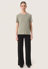 T-shirt a girocollo verde oliva abbinato a pantaloni larghi neri, entrambi realizzati in tessuto morbido, con una vestibilità rilassata e senza motivi visibili.