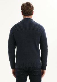 Maglione lavorato a maglia blu scuro con una texture a coste sulla parte superiore della schiena e sui polsini. Vestibilità regolare, con scollatura rotonda e maniche lunghe.