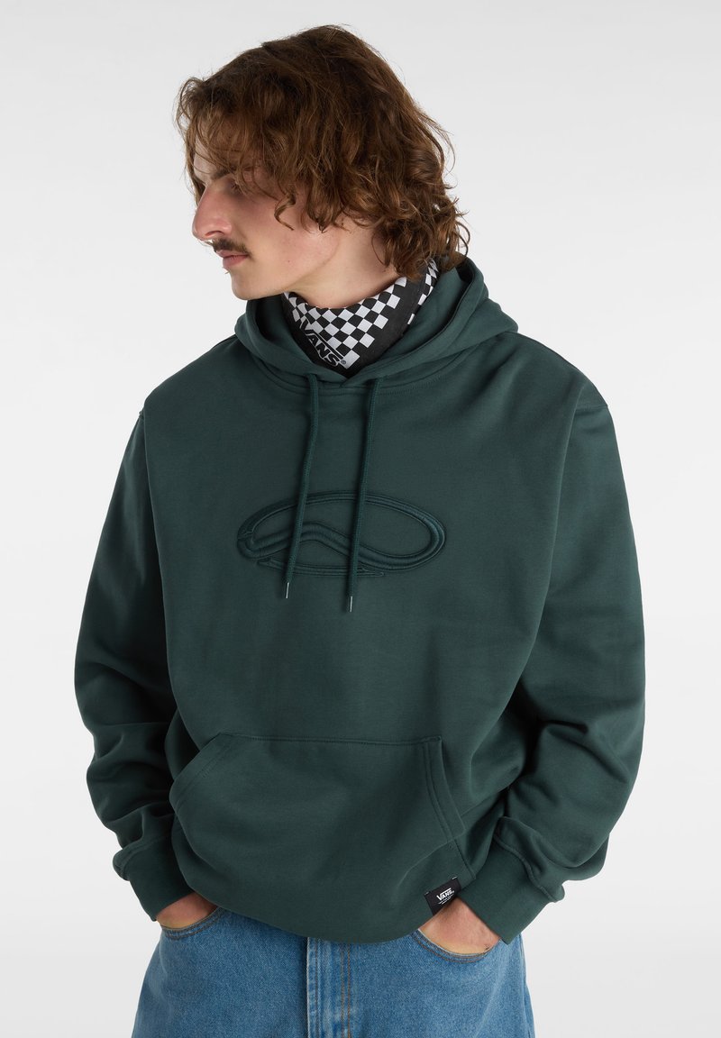 Felpa con cappuccio verde scuro con logo testurizzato, tasca a marsupio e cappuccio con coulisse. Indossata sopra una sciarpa a scacchi bianca e nera.
