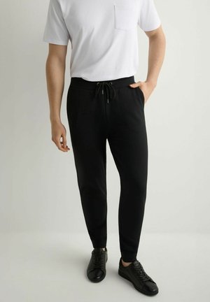 Czarne spodnie dresowe z talią na sznurek, o gładkiej fakturze i wąskim kroju. Zestawione z prostą białą koszulką i czarnymi trampkami.