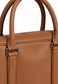 Bolso de cuero marrón texturizado con dos asas superiores, herrajes en tono plateado y marca grabada en el lateral. Forro interior suave.