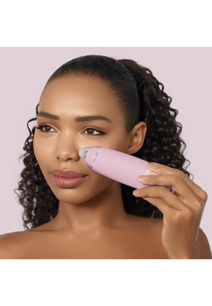Femme utilisant un aspirateur à pores facial rose sur le côté de son nez sur un fond violet clair.