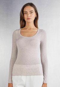 Hellgraues, langärmliges Oberteil aus weichem, strukturiertem Stoff mit einem runden Halsausschnitt und figurnahem Design, das an der Taille mit einem subtil helleren Band versehen ist.