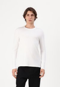 Hvid langærmet t-shirt i blødt stof, med rund hals og slim fit. Kombinationen med mørkfargede bukser. Enkel design uden mønstre.