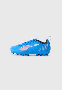 Botas de fútbol azules con parte superior sintética, que presentan una superficie texturizada, acentos negros, rayas naranjas y una pestaña en el talón. Clavos cortos en la suela.