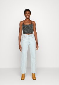 Top preto texturizado cortado com alças finas, combinado com jeans de perna reta de cintura alta em azul claro e sapatos de salto bloco amarelos.