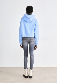 Sudadera corta de color azul claro con capucha y cordón, combinada con jeans ajustados grises y botas de tobillo blancas con un detalle negro.