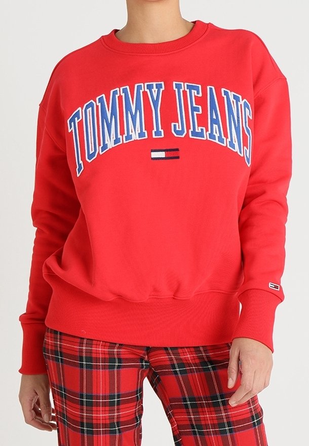 Personne portant un sweat-shirt rouge Tommy Jeans et un pantalon à carreaux rouges, avec le texte et le logo centrés sur le devant du sweat-shirt.