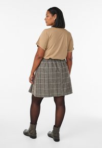 Beige Kurzarmoberteil, grauer Karorock mit weißen Linien, plissiertes Design und schwarze Stiefeletten. Glattes Material und strukturierte Silhouette.