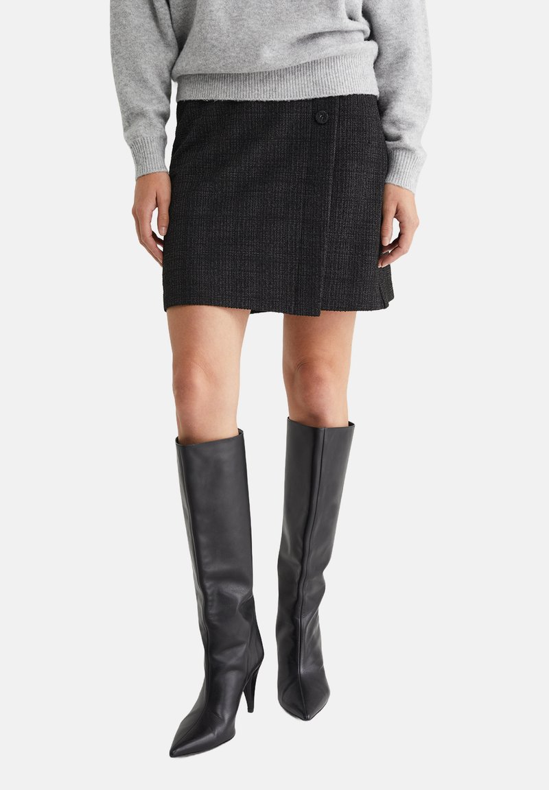 Falda negra texturizada con detalle de botones y corte recto, combinada con botas de cuero negro de tacón alto y puntera afilada.