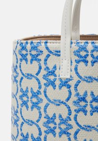 Tissu beige tissé avec broderie florale bleue sur un sac à main, avec des poignées en cuir blanc cousues sur le bord supérieur du sac.