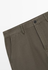 Pantalon vert olive avec fermeture à boutons, passants de ceinture, poches latérales et couture apparente sur tissu en coton.