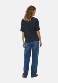 Mørkeblå kortærmet skjorte med lodrette folder, parret med lyseblå lige ben jeans. Outfittet har en afslappet pasform og blød tekstur.