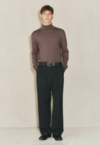 Brauner Rollkragenpullover mit glatter Textur, kombiniert mit hochgeschnittenen schwarzen Hosen und schwarzen Schuhen, die einen formellen Look kreieren.