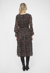 Svart blomstermønstret kjole med lange gjennomsiktige ermer, innsnevret midje og en flytende skjørt. Har små flerfargede blomsterdekorasjoner. Høye svarte støvler.