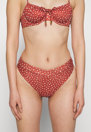 Conjunto de biquíni vermelho com bolinhas brancas, apresentando um topo com aros franzido e um laço, além de uma parte de baixo de cintura alta. Tecido de textura suave.