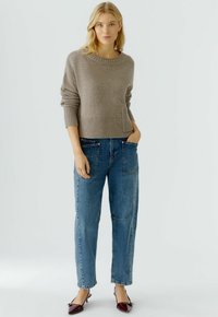 Lichtbruine gebreide trui met een geribbelde onderkant en mouwen, gecombineerd met blauwe denim jeans in een relaxed fit en met voorzakken.