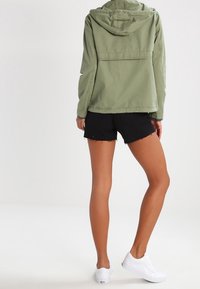 Olivengrøn hættetrøje med en afslappet pasform, kombineret med sorte slidte shorts. Hvide sneakers fuldender outfittet.