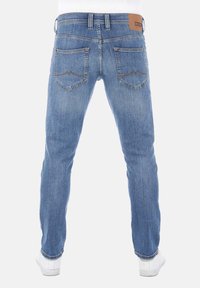 Jeans de mezclilla azul claro con corte recto, que cuentan con dos bolsillos traseros y una etiqueta de cuero marrón en la cinturilla. Zapatillas blancas.