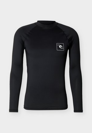 Maglietta sportiva nera a maniche lunghe con scollo rotondo e piccolo logo ondulato bianco all'interno di un quadrato sul petto sinistro, su sfondo grigio.