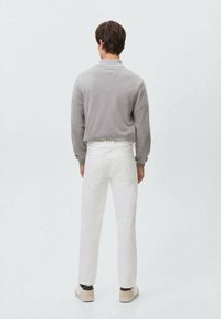 Suéter gris con un corte relajado, pantalones claros y zapatillas beige. La tela parece suave; los pantalones tienen bolsillos traseros.