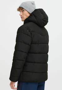 Jachetă puf cu capotă de culoare neagră, cu segmente cusute orizontal. Materialul pare neted, iar designul este elegant și modern.