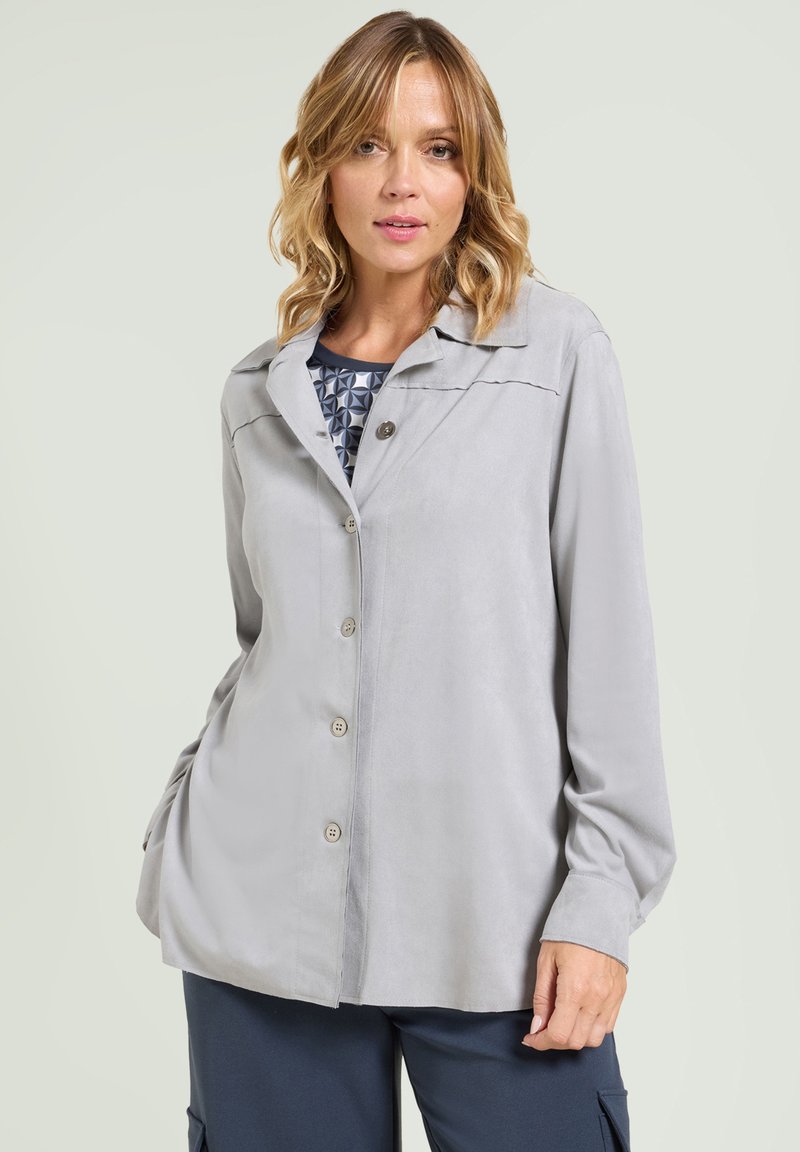 Jasnoszara, zapinana bluzka z miękkiego, gładkiego materiału, z kołnierzykiem w kształcie litery V i długimi rękawami. Płaskie szwy dodają szczegółów.