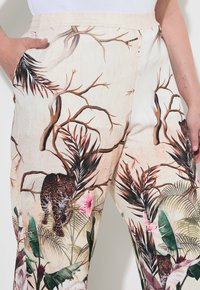 Pantaloni a vestibilità comoda con una base crema, caratterizzati da una vivace stampa di giungla che presenta leopardi, fogliame e accenti floreali nei toni del verde, rosa e marrone.